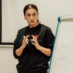 Woman confidently presenting with a flip chart in a classroom setting.